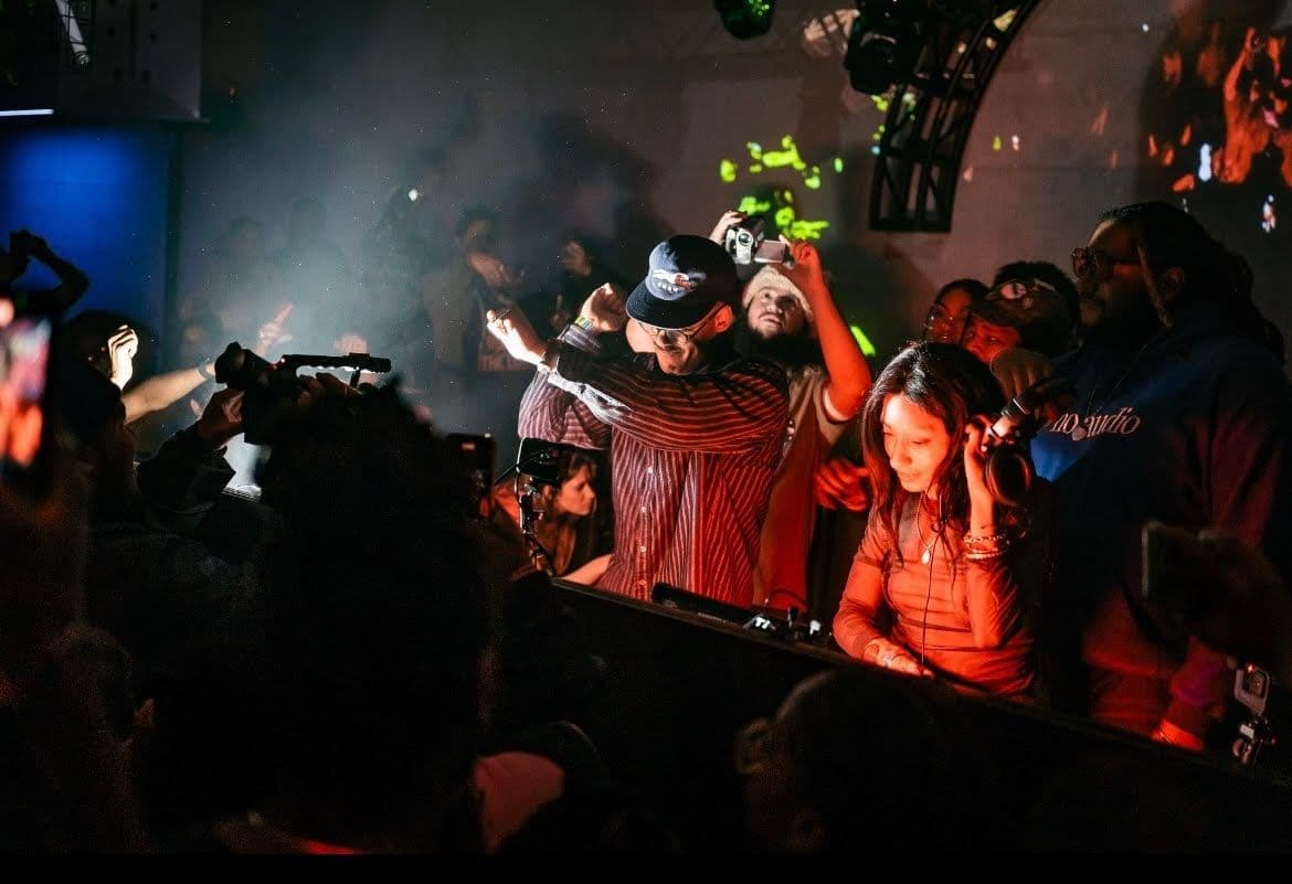 A DJ at the center playing music at a nightclub surrounded by partygoers.