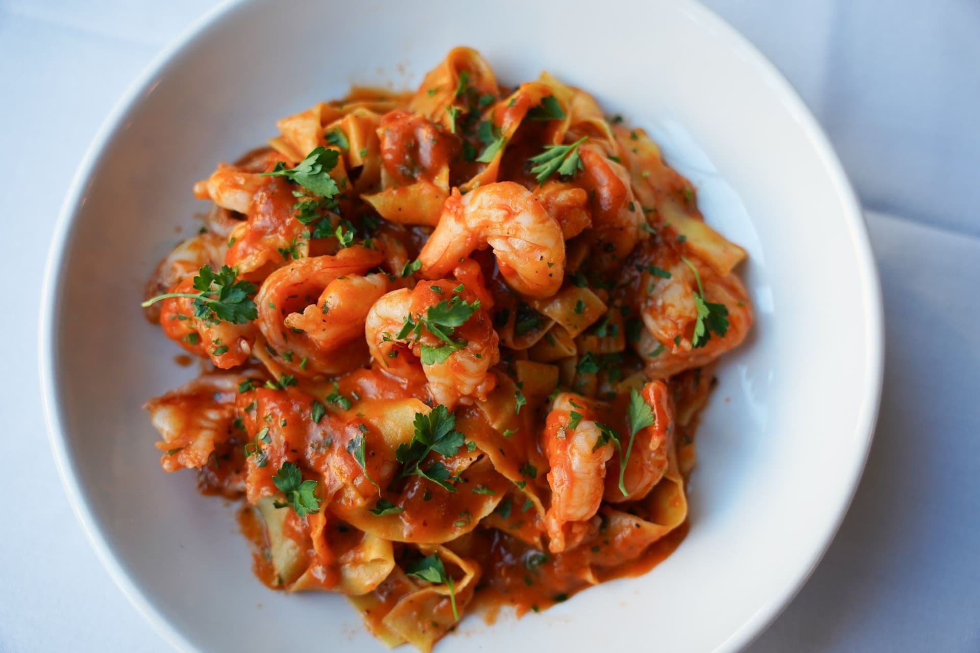 Shrimp pasta sprinkled with parsley on a white plate and white tablecloth
