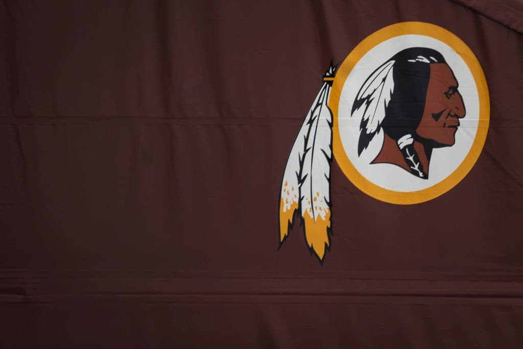 A brown flag with a decommissioned logo for the Washington Commanders depicting a Native American person with feathers.