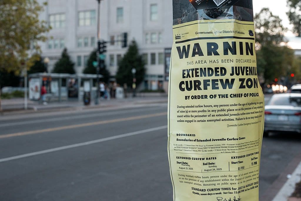 A photo of a sign with a curfew zone notice plastered on it.