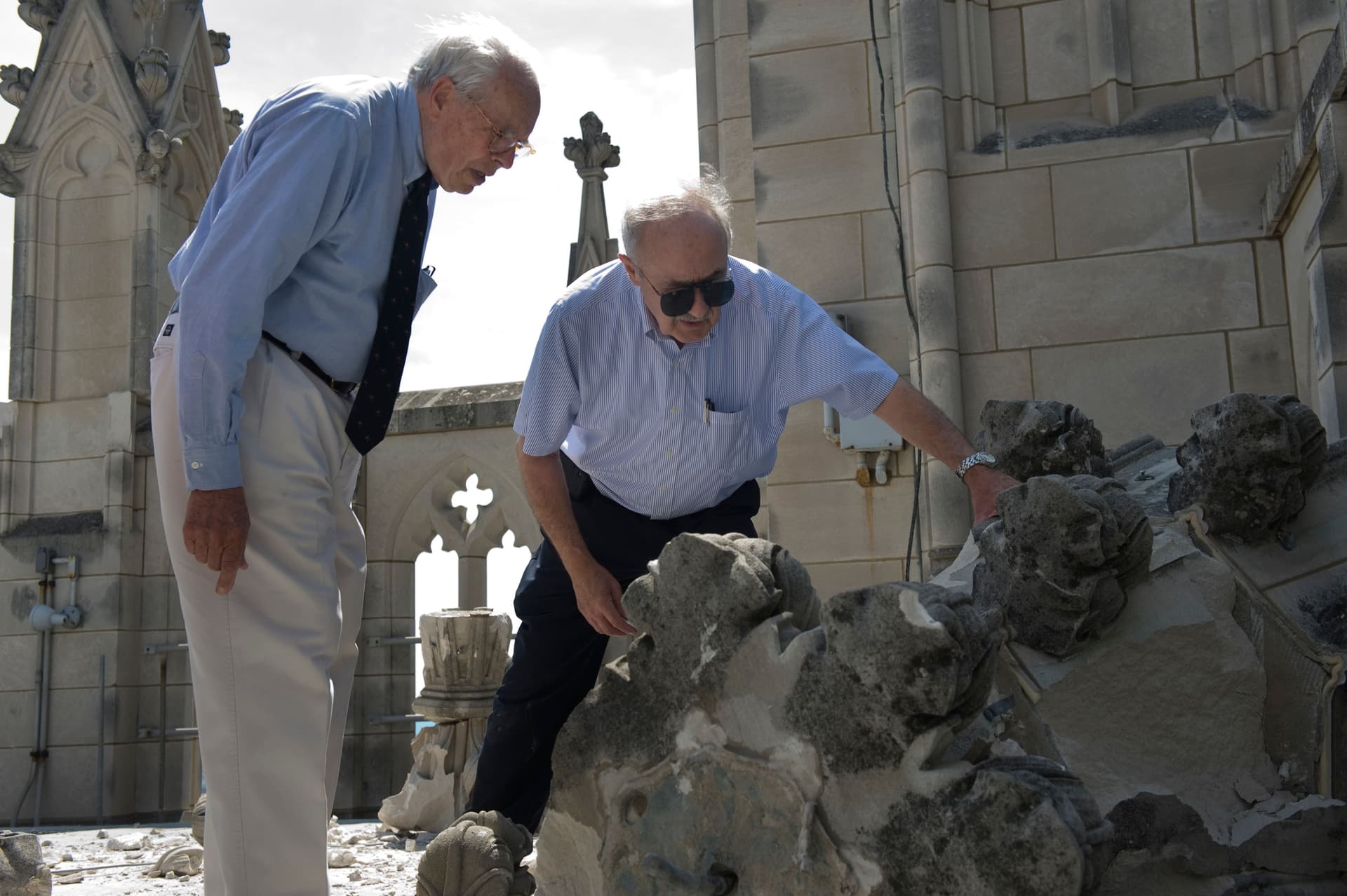 wo men in blue collared shirts survey the damage to the National Cathedral after an earthquake.